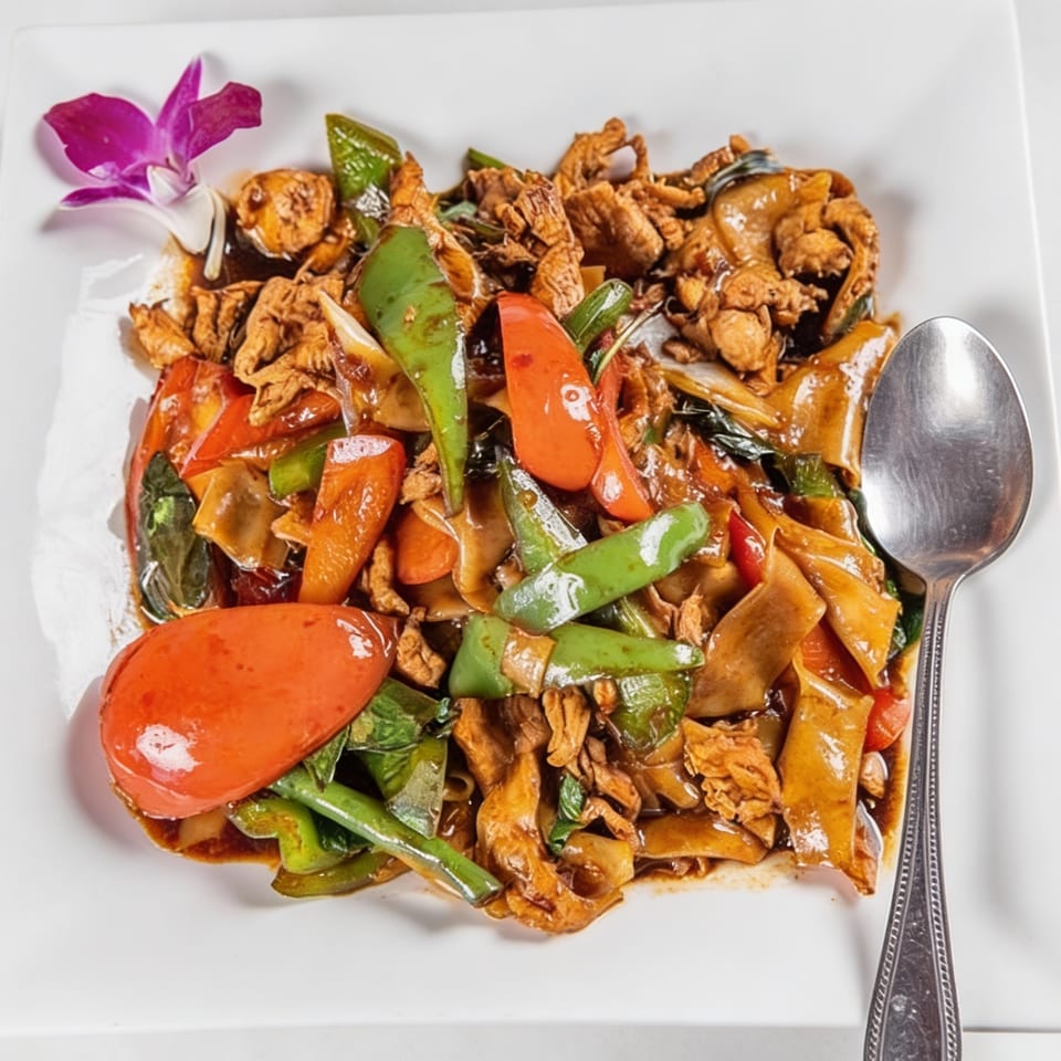 Thai Drunken Noodles with chicken, red and green bell peppers, and a purple orchid garnish.